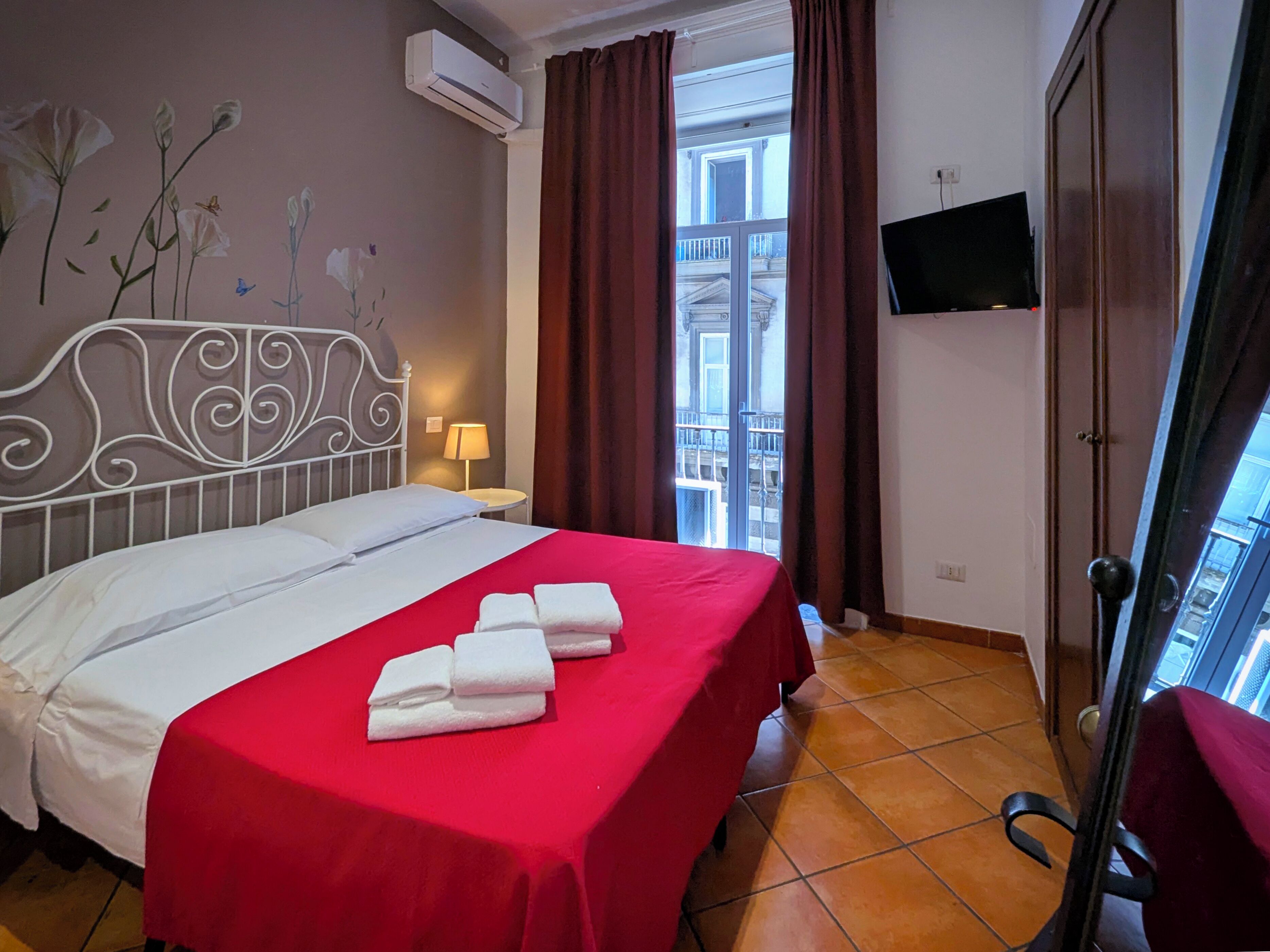 A hotel room with a bed, a TV mounted on the wall, and a view of the outside balcony.