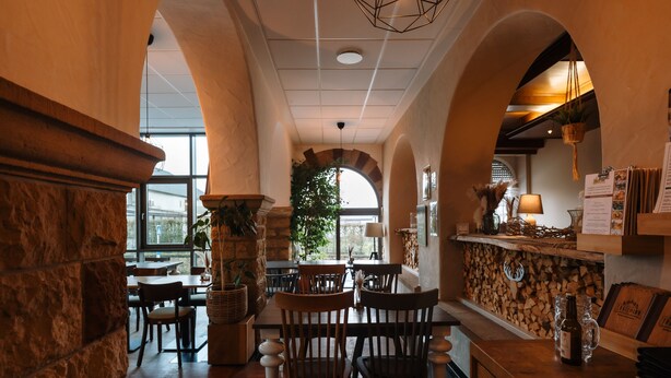 Um restaurante acolhedor com paredes de pedra, mobiliário de madeira e uma grande janela com vista para o exterior.