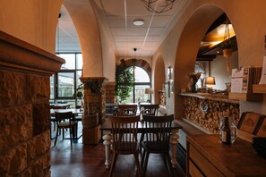 A cozy restaurant with stone walls, wooden furniture, and a large window offering a view of the outdoors. - Trail-Inn Natur & Sporthotel (Berdorf)