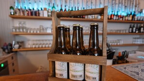 Uma caixa de madeira com quatro garrafas de cerveja, rótulos com a inscrição "Vandergenoss Trail Inn".
