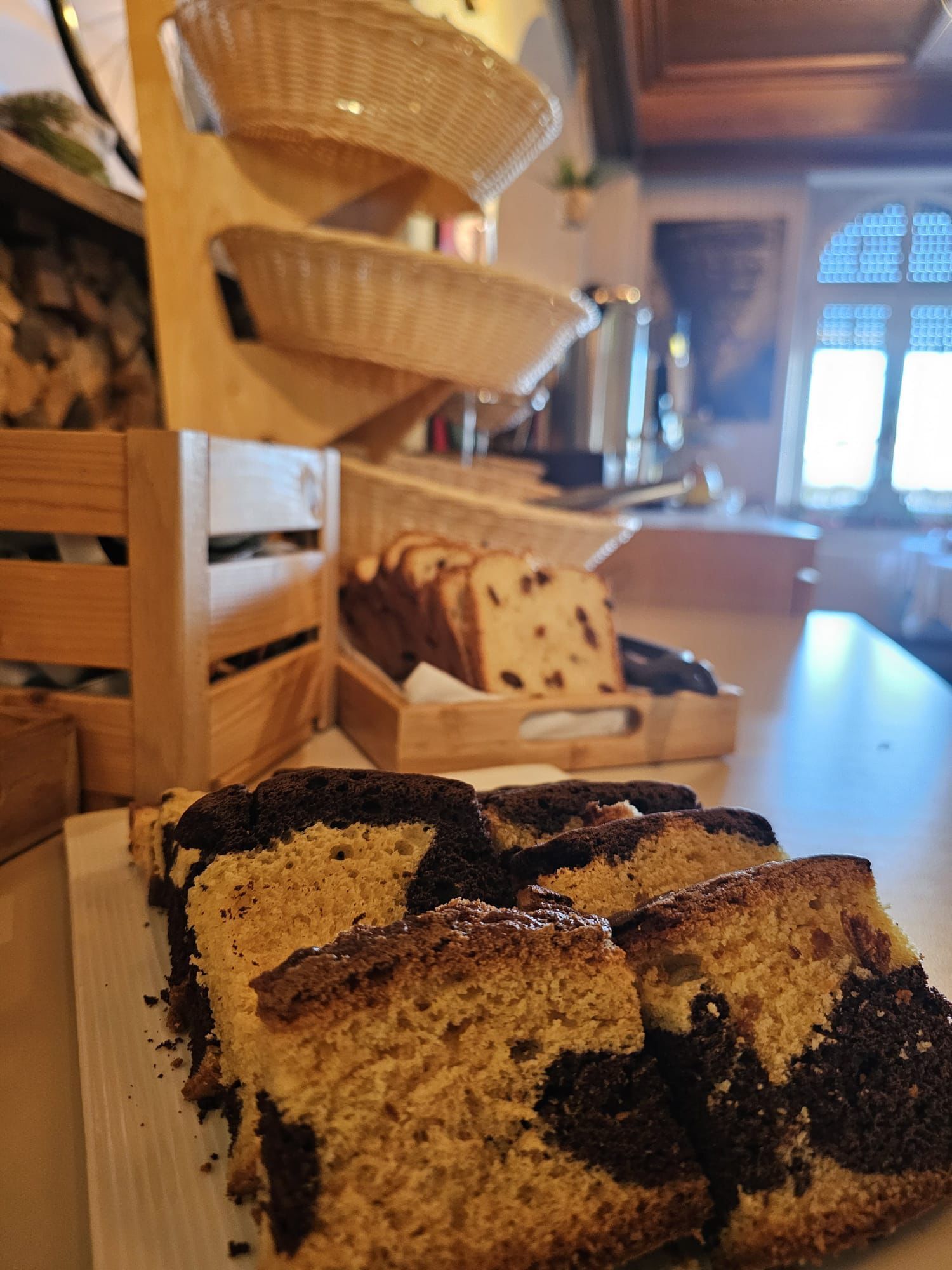 A bakery display with various baked goods, including cakes and bread, arranged on wooden stands and a white plate.