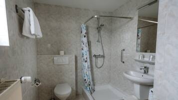 Een badkamer met douche, toilet, wastafel en spiegel.