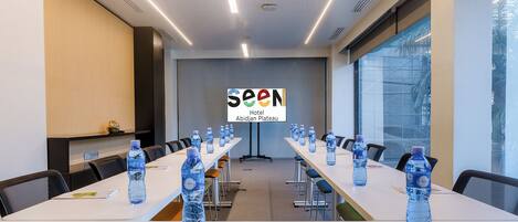 A conference room with long tables, water bottles, and a 'SEEN Hotel Abidjan Plateau' sign.