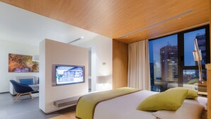 Una habitación de hotel moderna con una cama grande, televisión, escritorio con silla y vistas a la ciudad.