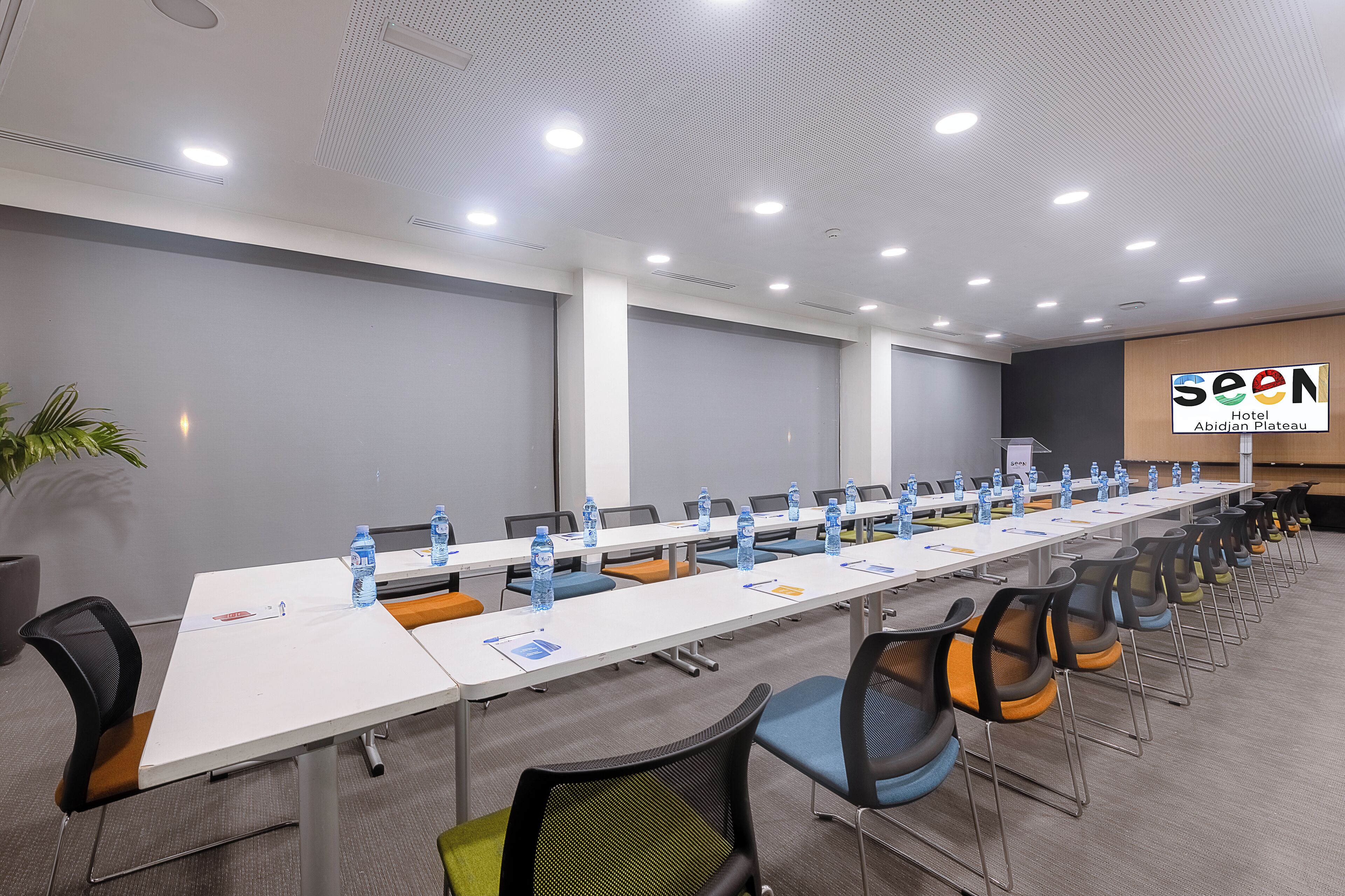 Un salón de conferencias con una larga mesa, sillas, botellas de agua y un logotipo en la pared.