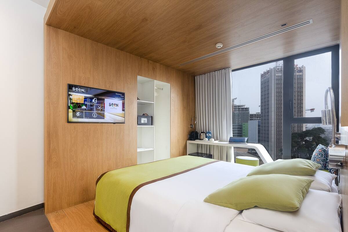 A hotel room with a bed, a desk, a TV, and a view of the city.