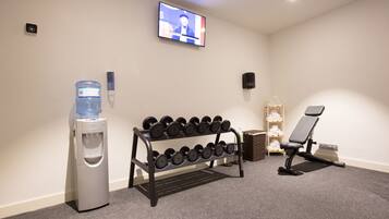 A gym with a water dispenser, dumbbell rack, exercise chair, and a TV on the wall.