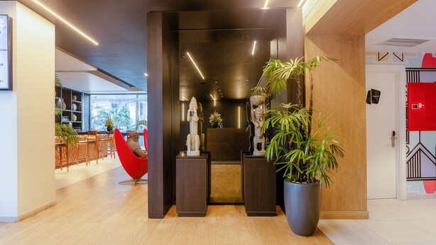 Un vestíbulo moderno con mostrador de recepción de madera, una silla roja y plantas en macetas.
