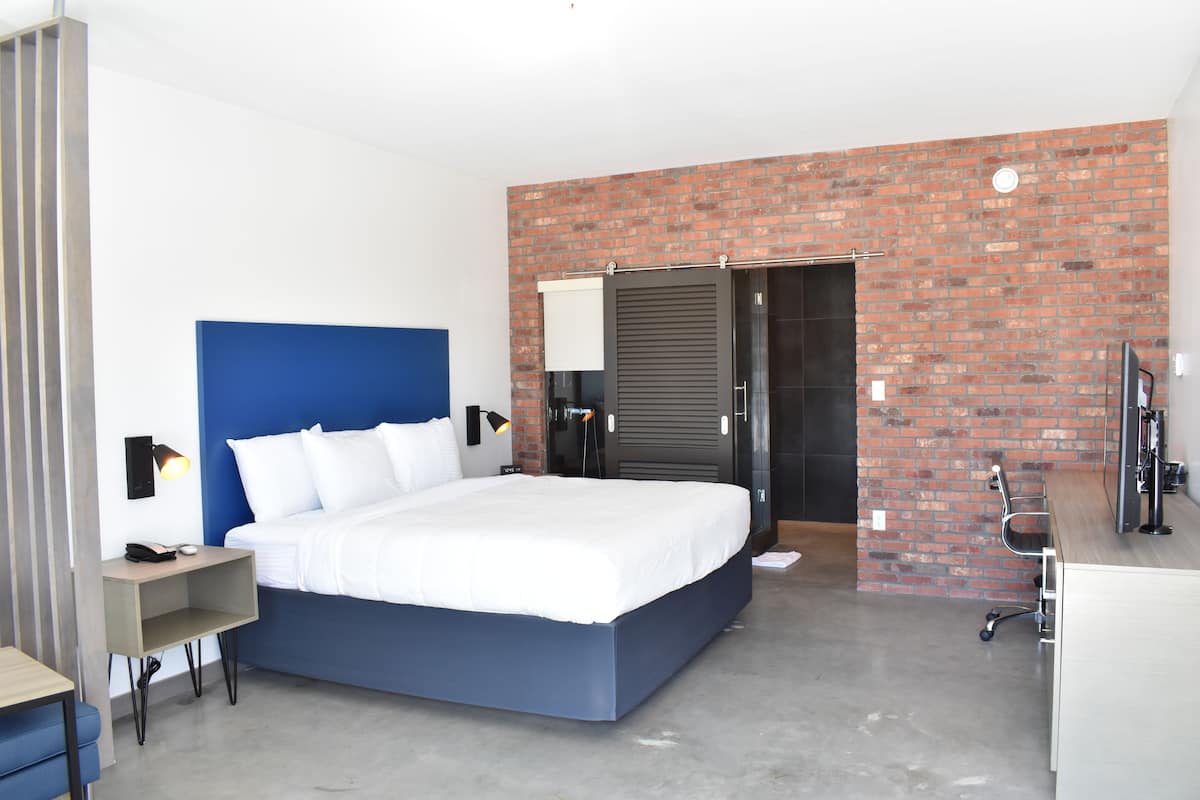 Una habitación de hotel moderna con una cama grande, un escritorio, una computadora y una pared decorativa de ladrillo.