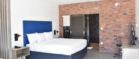 Een moderne hotelkamer met een groot bed, een bureau, een computer en een wand met bakstenen.
