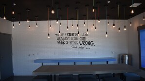 Un interior moderno con una larga mesa y sillas, un muro de ladrillo blanco y lámparas colgantes.