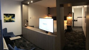 Zona de recepción de un hotel con un mostrador, un televisor mostrando 'TRowePhic' y un área de descanso con sillas.