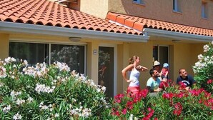 Un bâtiment avec un toit recouvert de tuiles rouges et une façade jaune, entouré de plantes en fleurs.