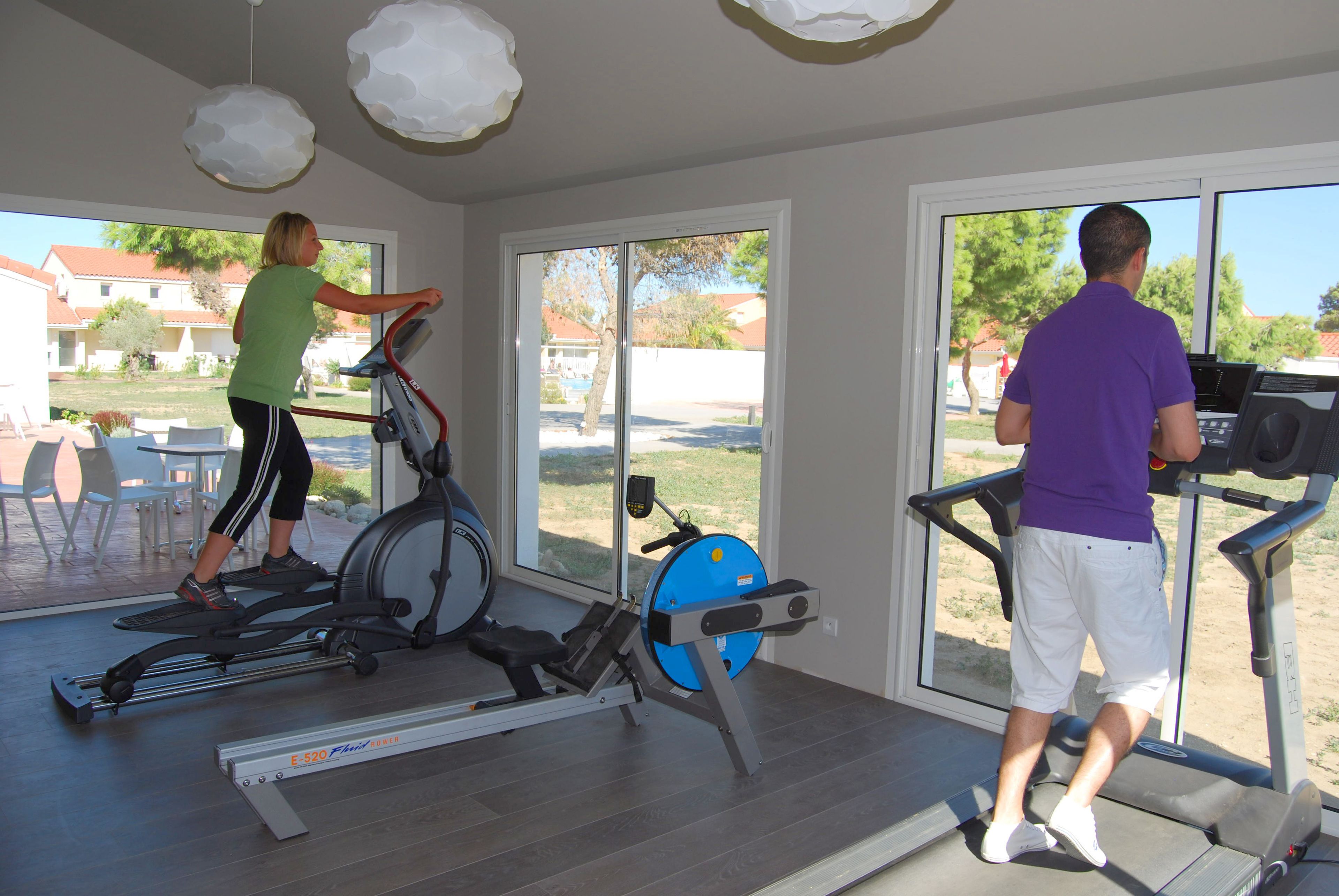 Une salle de sport à domicile équipée de matériel d’exercice, dotée de grandes fenêtres et offrant une vue sur le quartier.