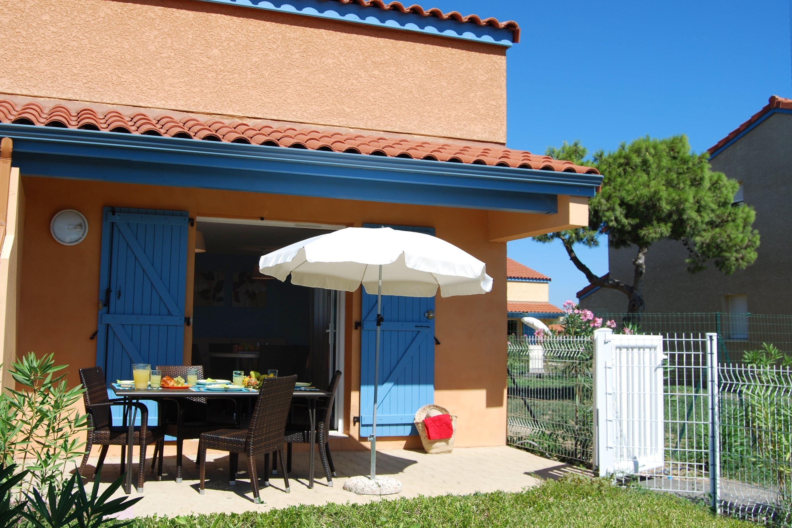 A patio with a table and chairs, a blue door, and a white umbrella.