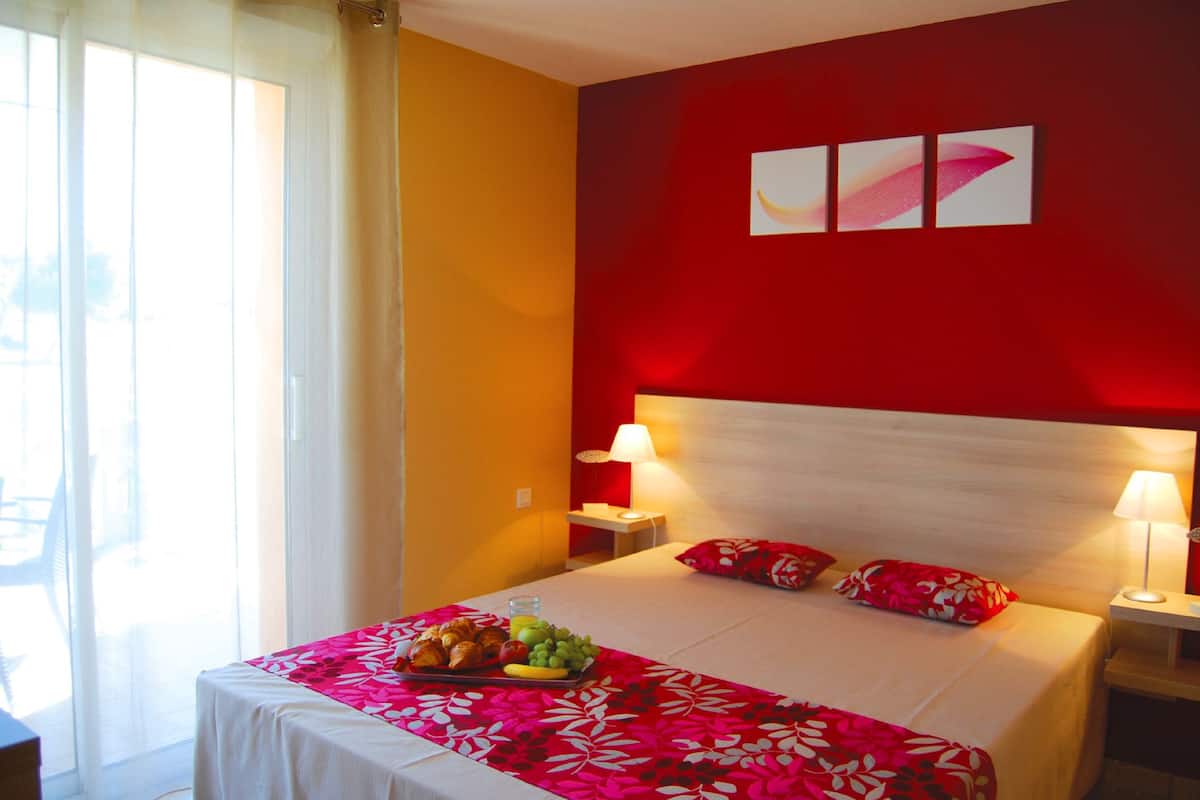 Een hotelkamer met een bed, twee bedlampen, een ontbijttafel en een rode accentmuur.