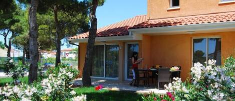 A two-story house with a tiled roof, a patio with outdoor furniture, and a garden with various flowers.