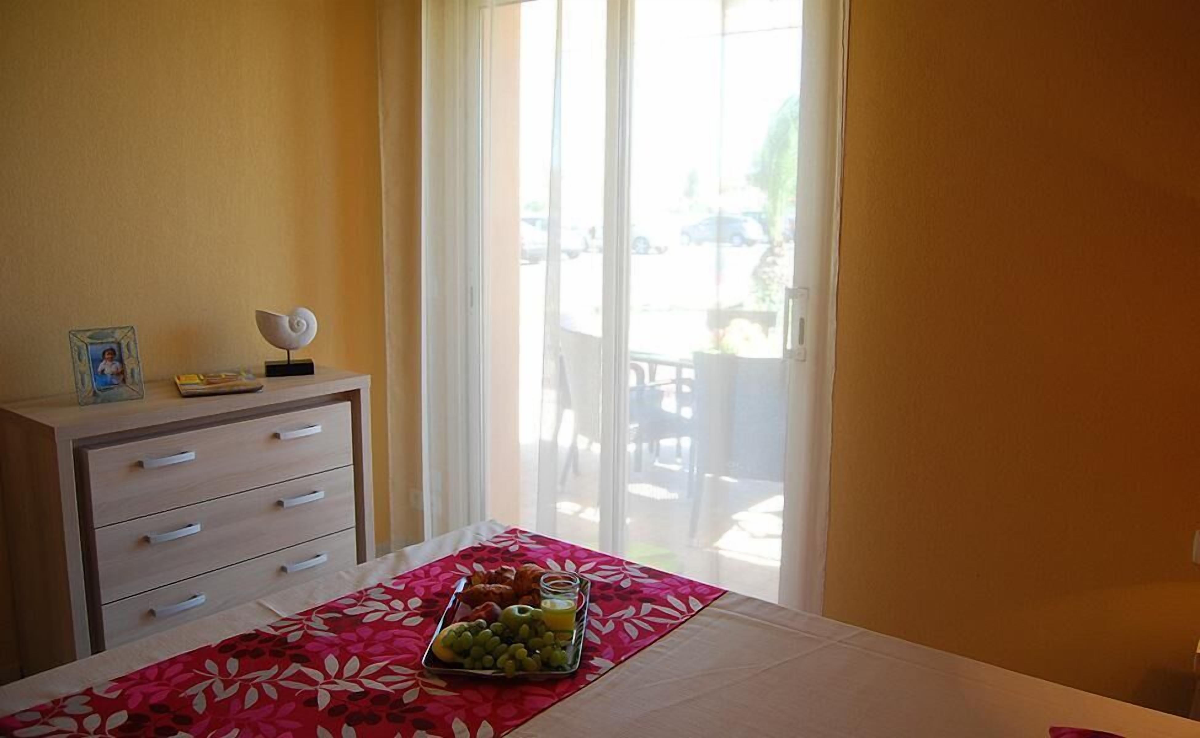 A hotel room with a bed, a dresser, and a table with a fruit tray.