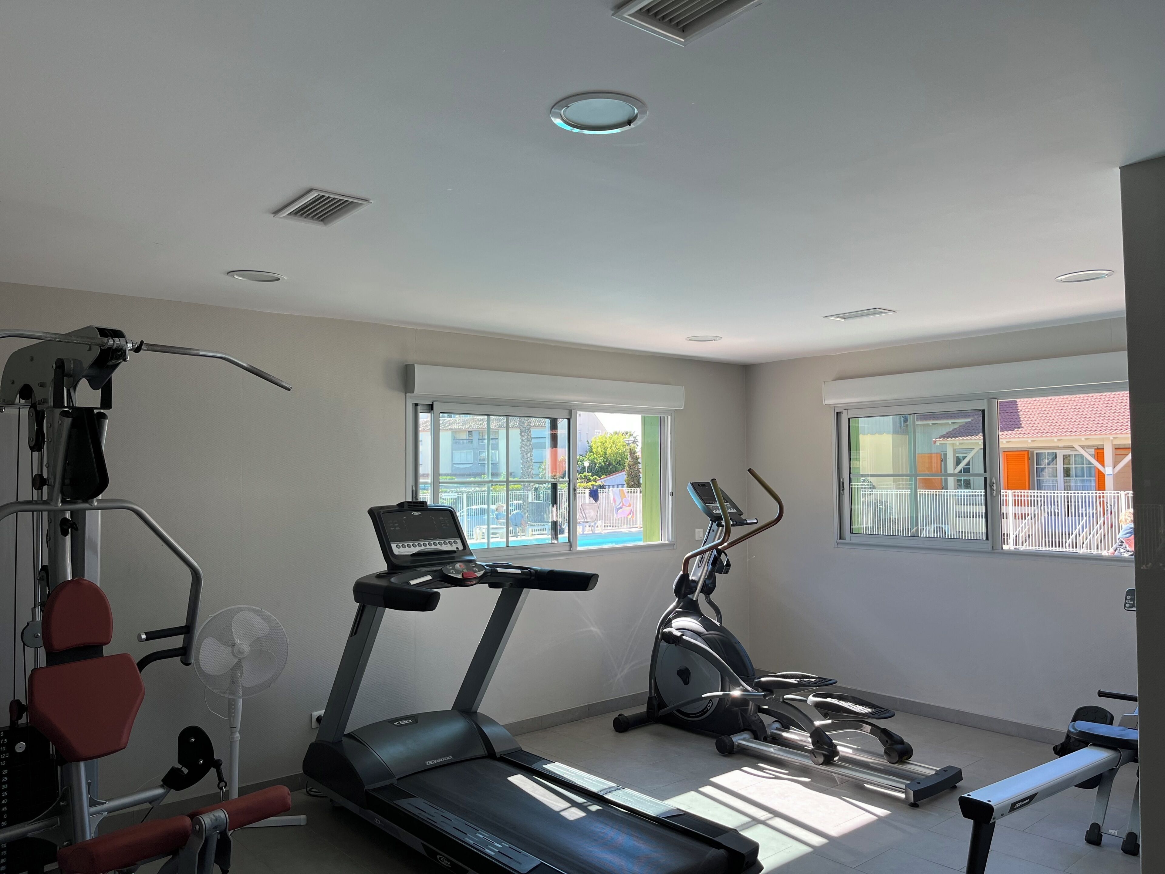 A gym with exercise equipment, large windows, and a view of the outside.