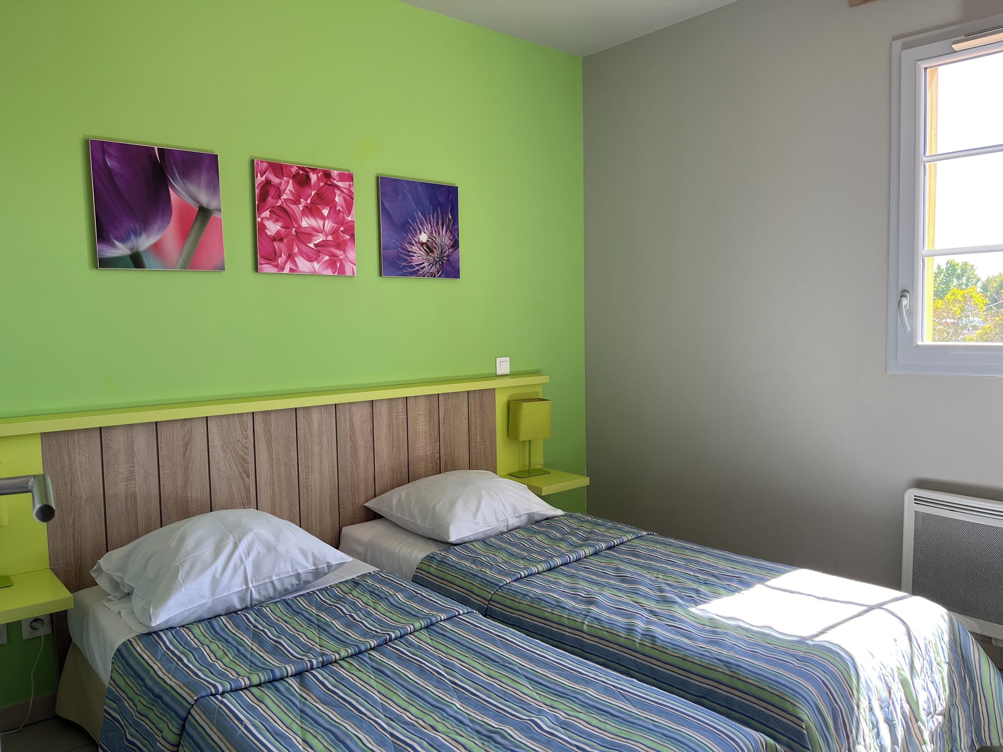 A room with two beds, a wooden headboard, a green wall, and three framed floral paintings.