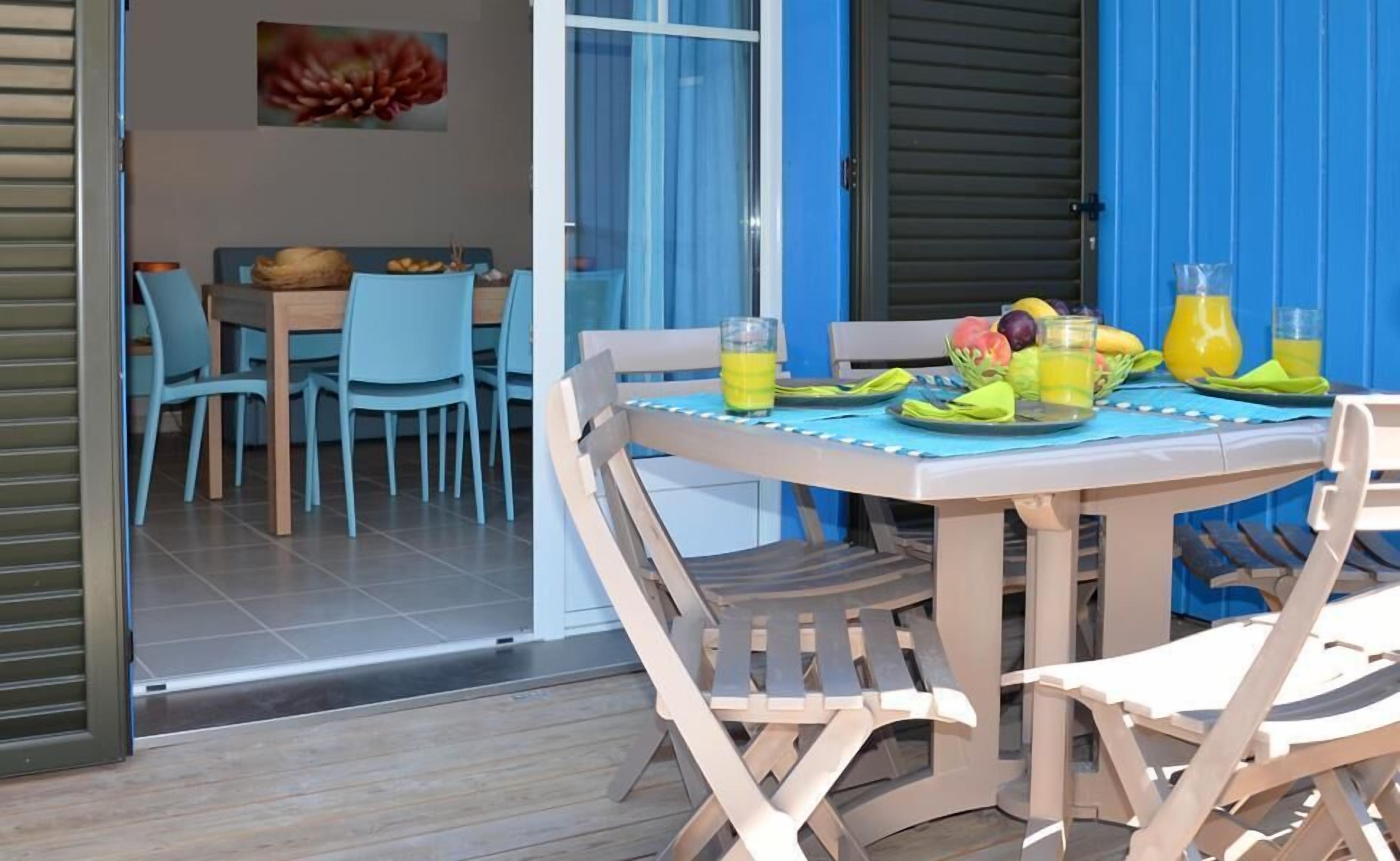 An outdoor dining area with a table set for two, chairs, and a fruit basket.