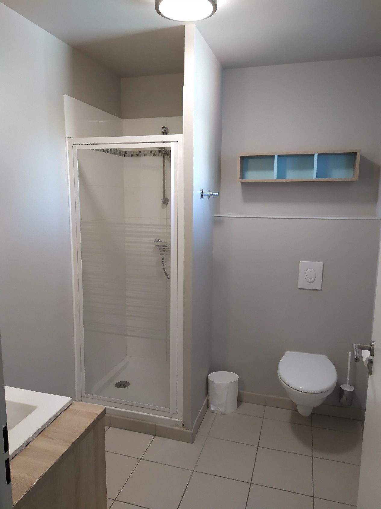 Ein Badezimmer mit Dusche, Toilette und Ablage über der Toilette.