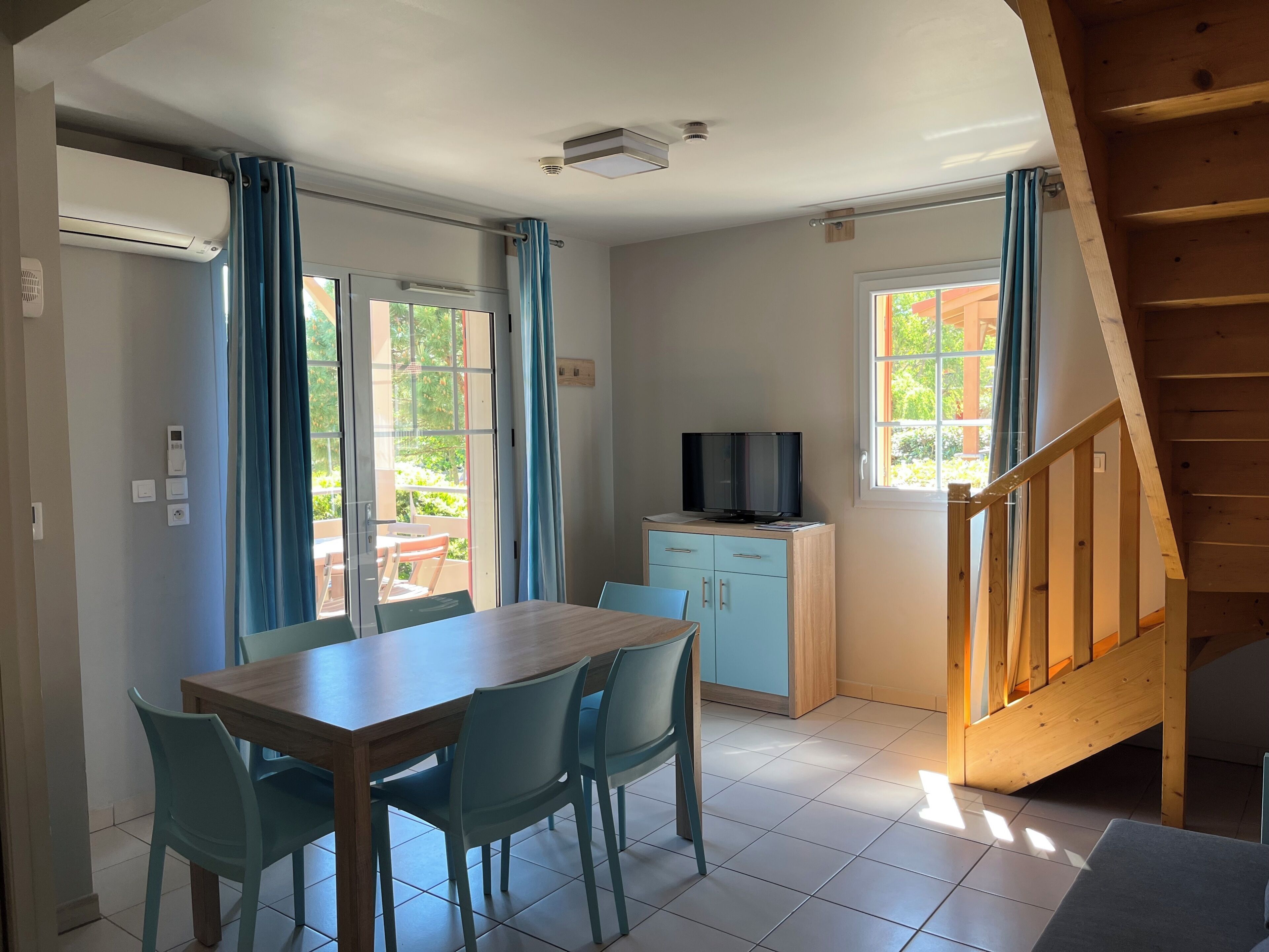 Een kamer met een eettafel, stoelen, een televisie op een kast en een trap.
