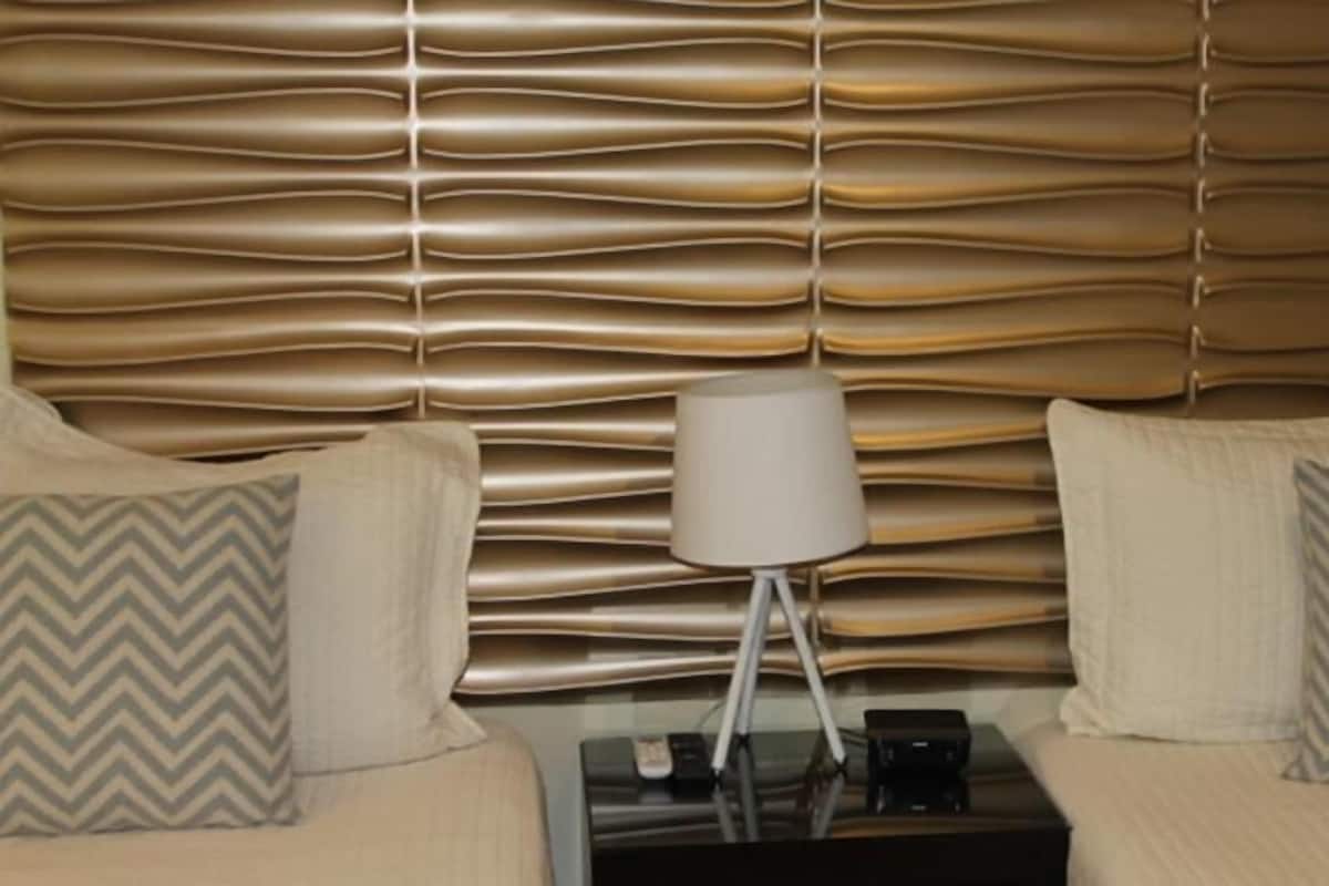 A hotel room with a textured headboard, a bedside table with a lamp, and two patterned pillows.