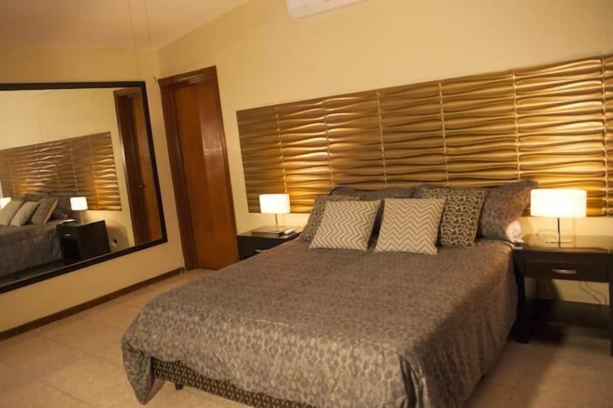 A hotel room with a large bed, a mirror, two bedside tables, and a headboard with horizontal slats.