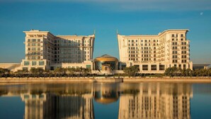 A large, modern hotel with a central dome structure, multiple floors, and a reflection in the water in front. - The St. Regis Astana (Astana)