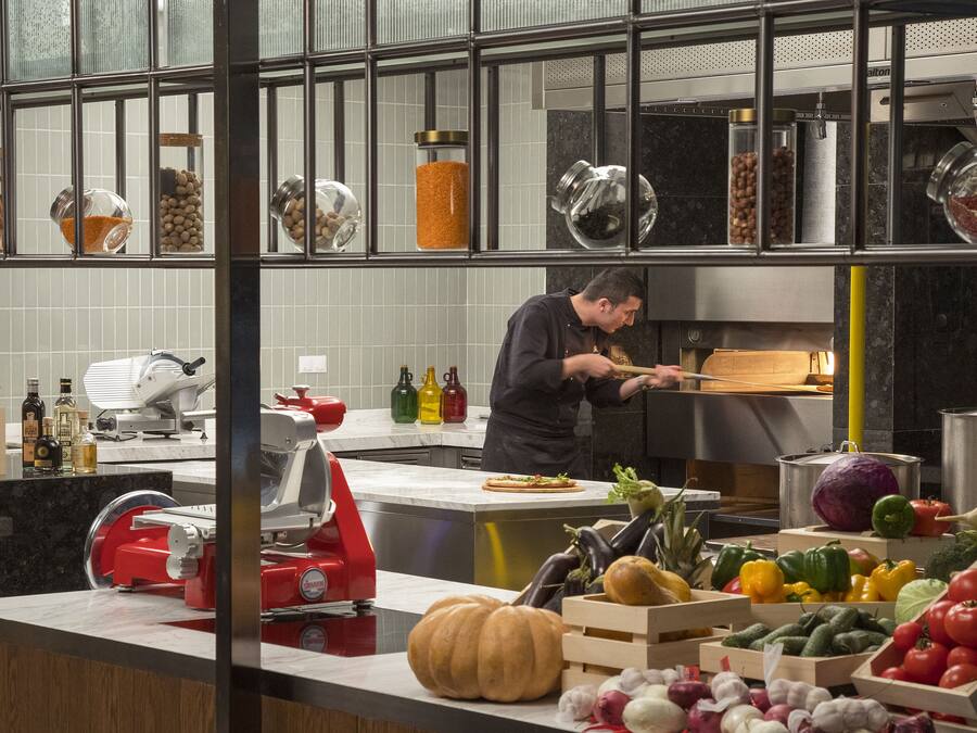 A kitchen with a chef preparing food, various kitchen appliances, and a display of fresh produce.