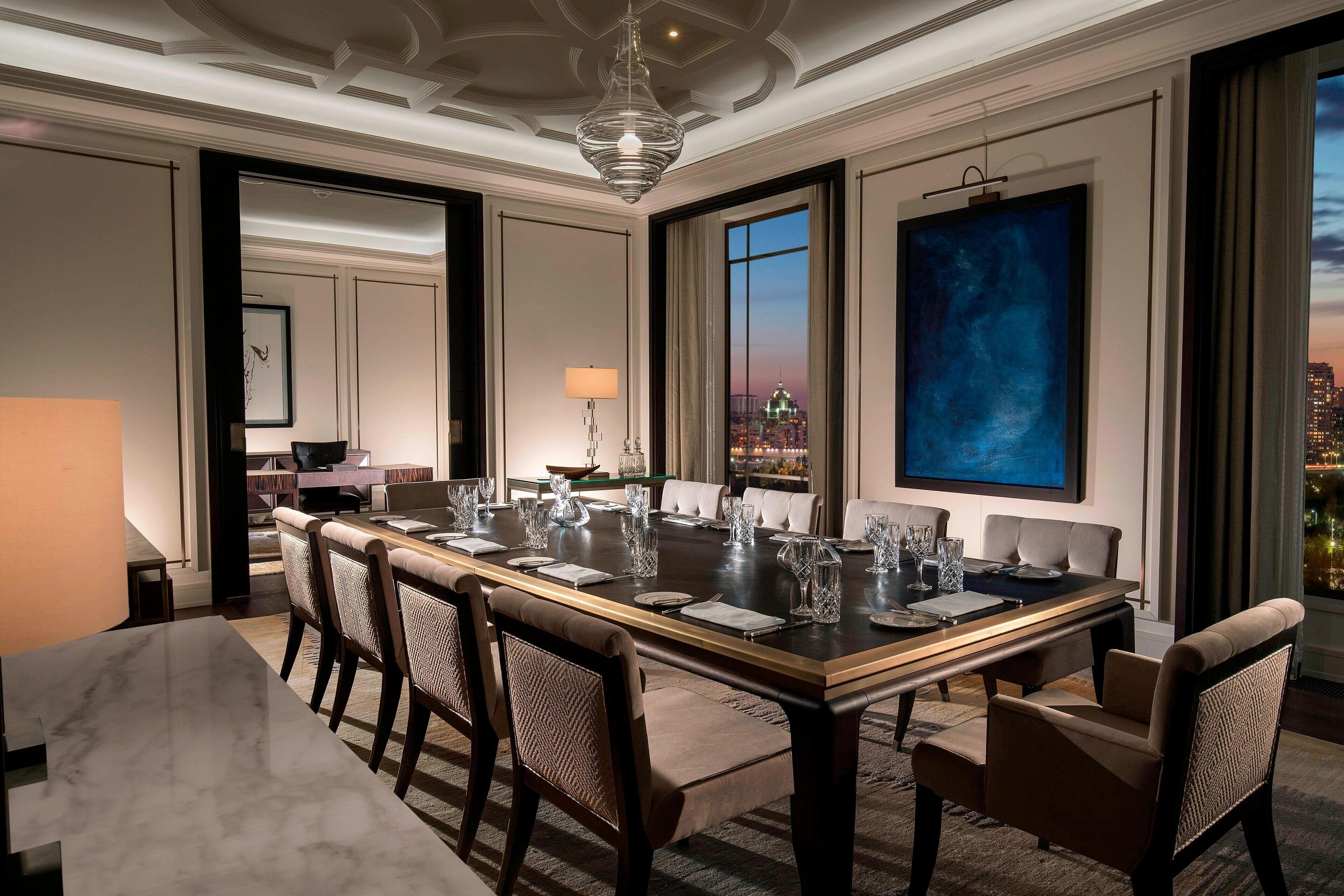 A spacious dining area with a long table set for a meal, surrounded by upholstered chairs.