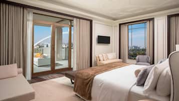 A hotel room with a large bed, a sofa, a chair, a TV, and a balcony with a city view.
