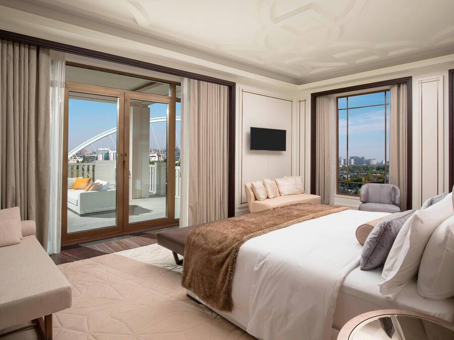 A hotel room with a large bed, a sofa, a chair, a TV, and a balcony with a city view.