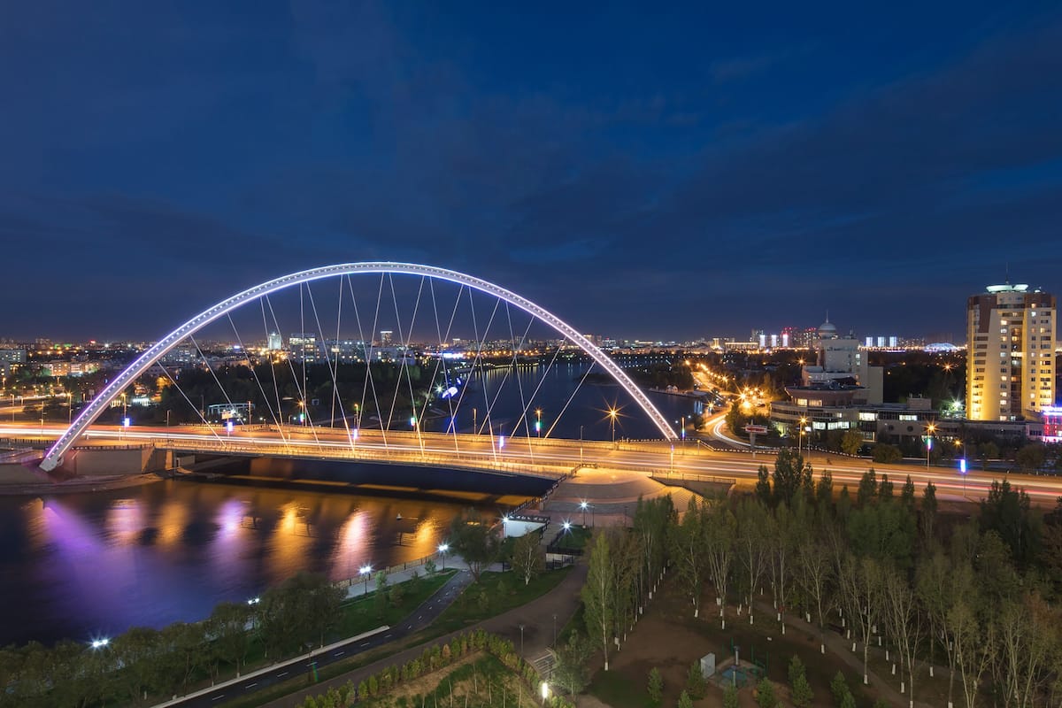 Eine Skyline mit einer markanten, beleuchteten Brücke, Hochhäusern und einem Fluss.