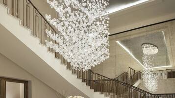 A grand staircase with a modern chandelier, marble flooring, and a seating area with a table and chairs.