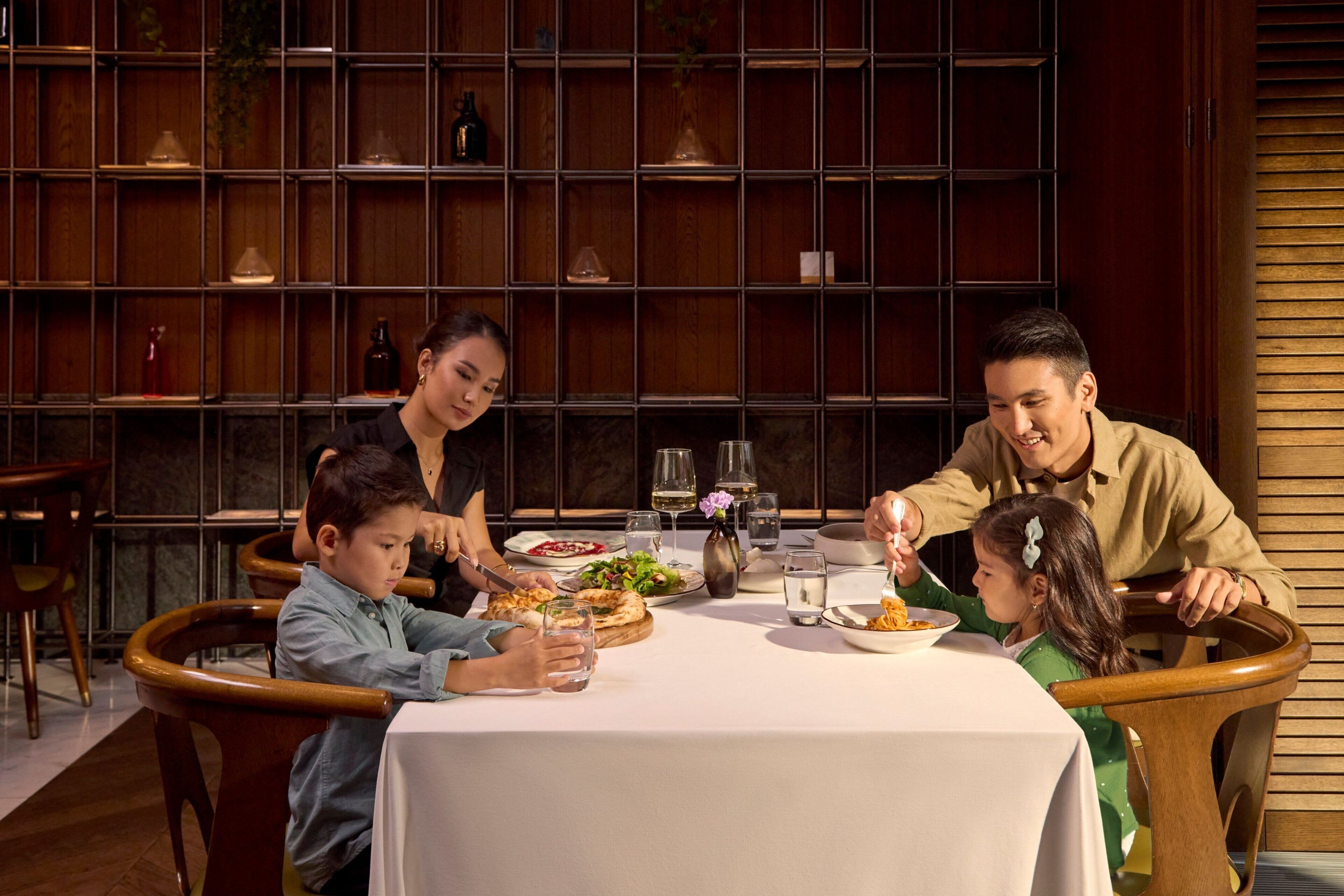 A family dining at a table with a white tablecloth, surrounded by wooden chairs.