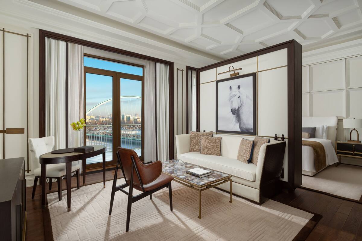 Ein modernes Hotelzimmer mit großem Fenster, einer Couch, einem Couchtisch, einem Sessel und einem Bett.