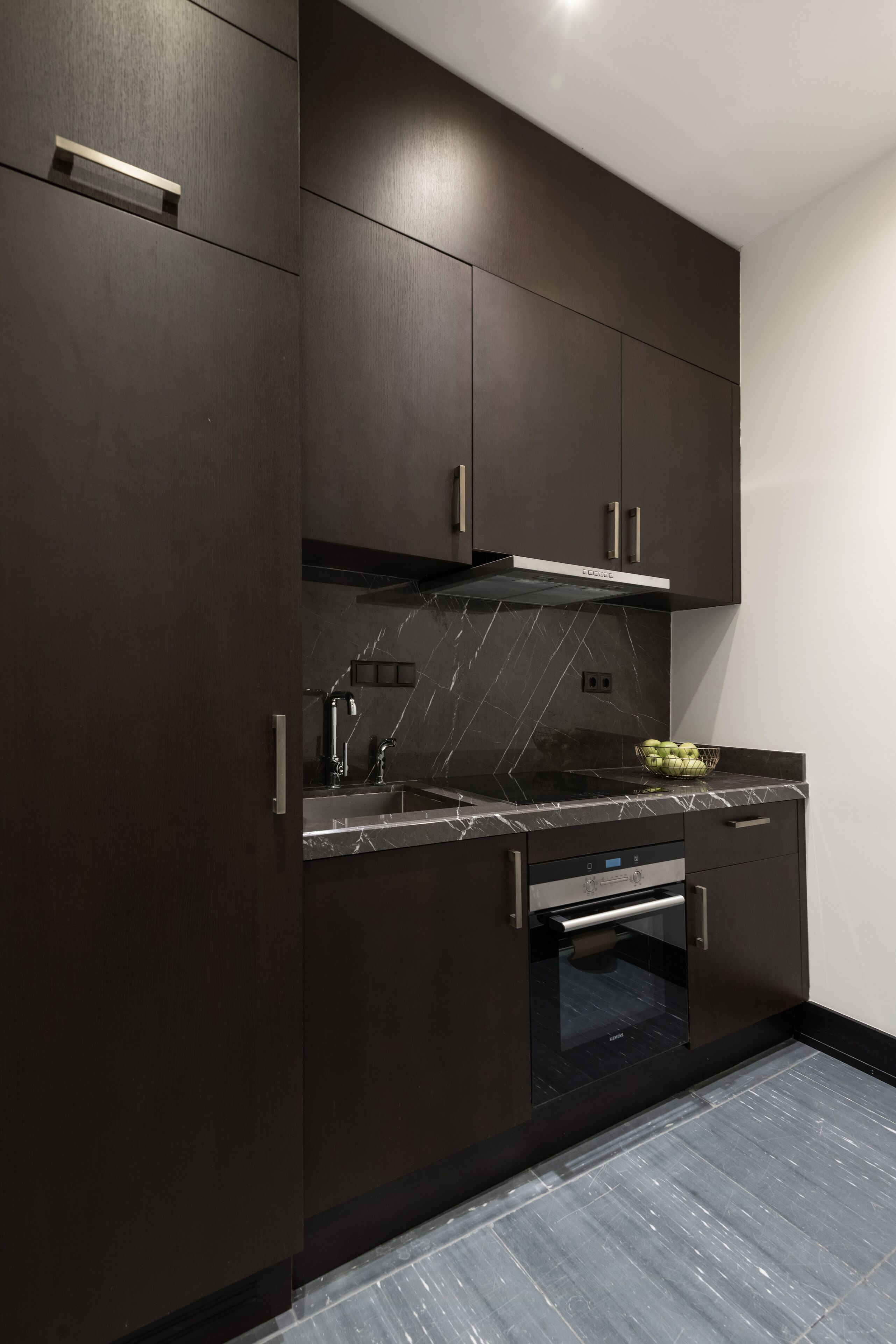 Una cocina moderna con muebles oscuros, encimera de mármol y horno empotrado.