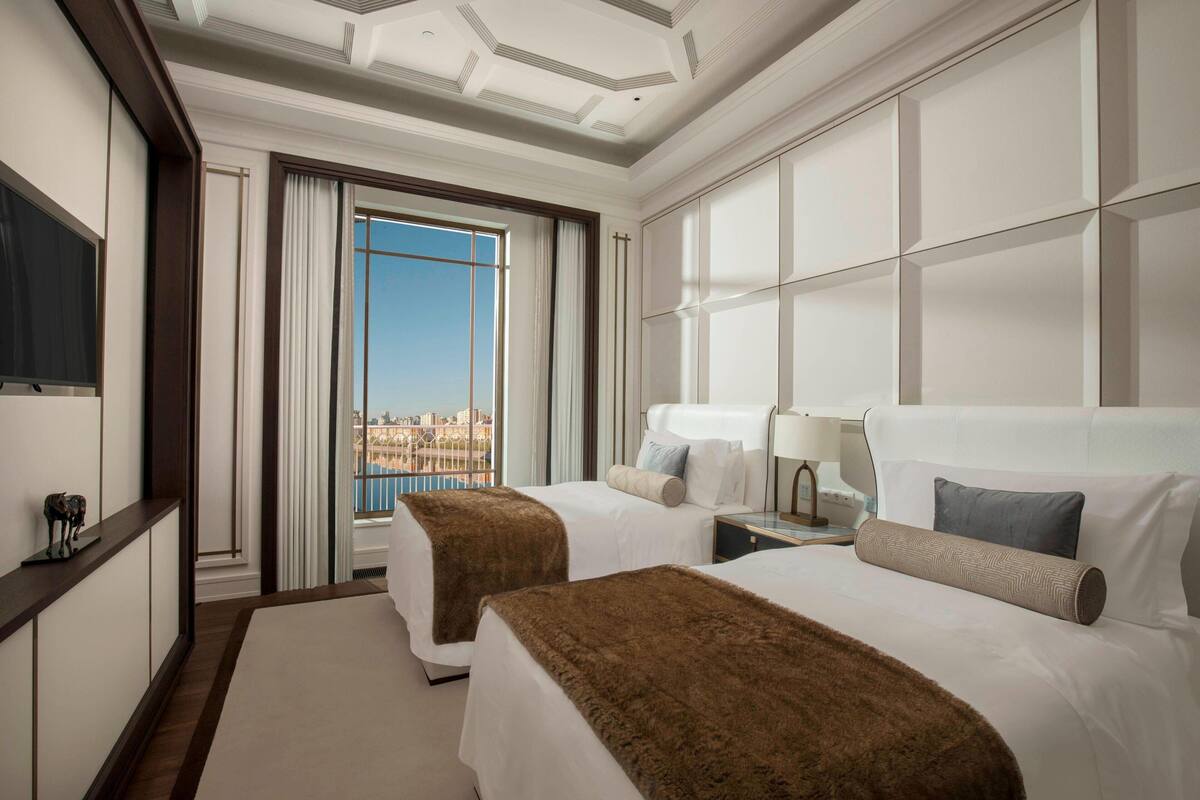 Ein Hotelzimmer mit zwei Betten, einem großen Fenster mit Stadtblick, einem Flachbildfernseher und einem Nachttisch mit Lampe.