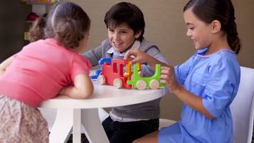 Three children playing with toy trains at a round table.