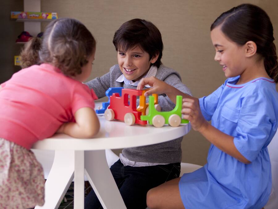 Three children playing with toy trains at a round table.