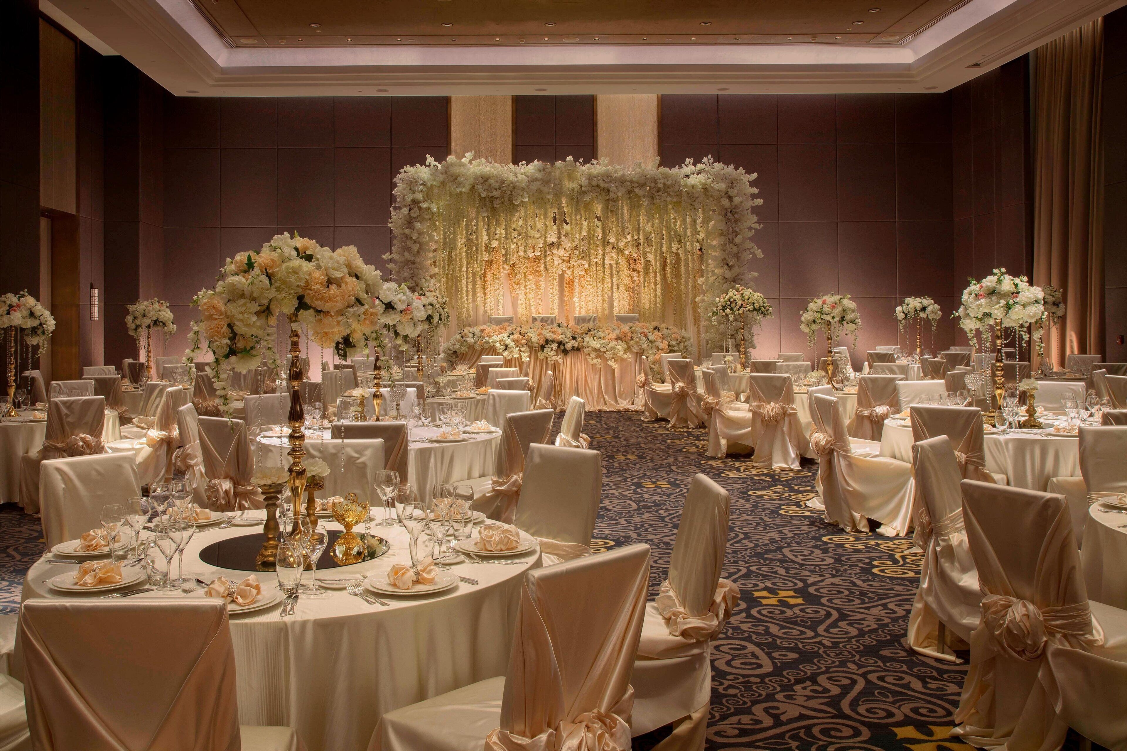 A banquet hall with round tables, white tablecloths, and chairs with white covers.