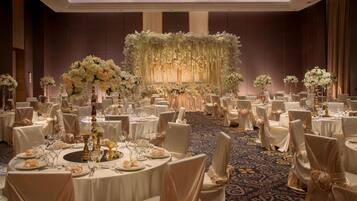 A banquet hall with round tables, white tablecloths, and chairs with white covers.