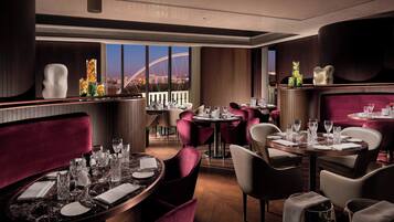 A restaurant with round tables, red upholstered chairs, and a view of a bridge and cityscape.