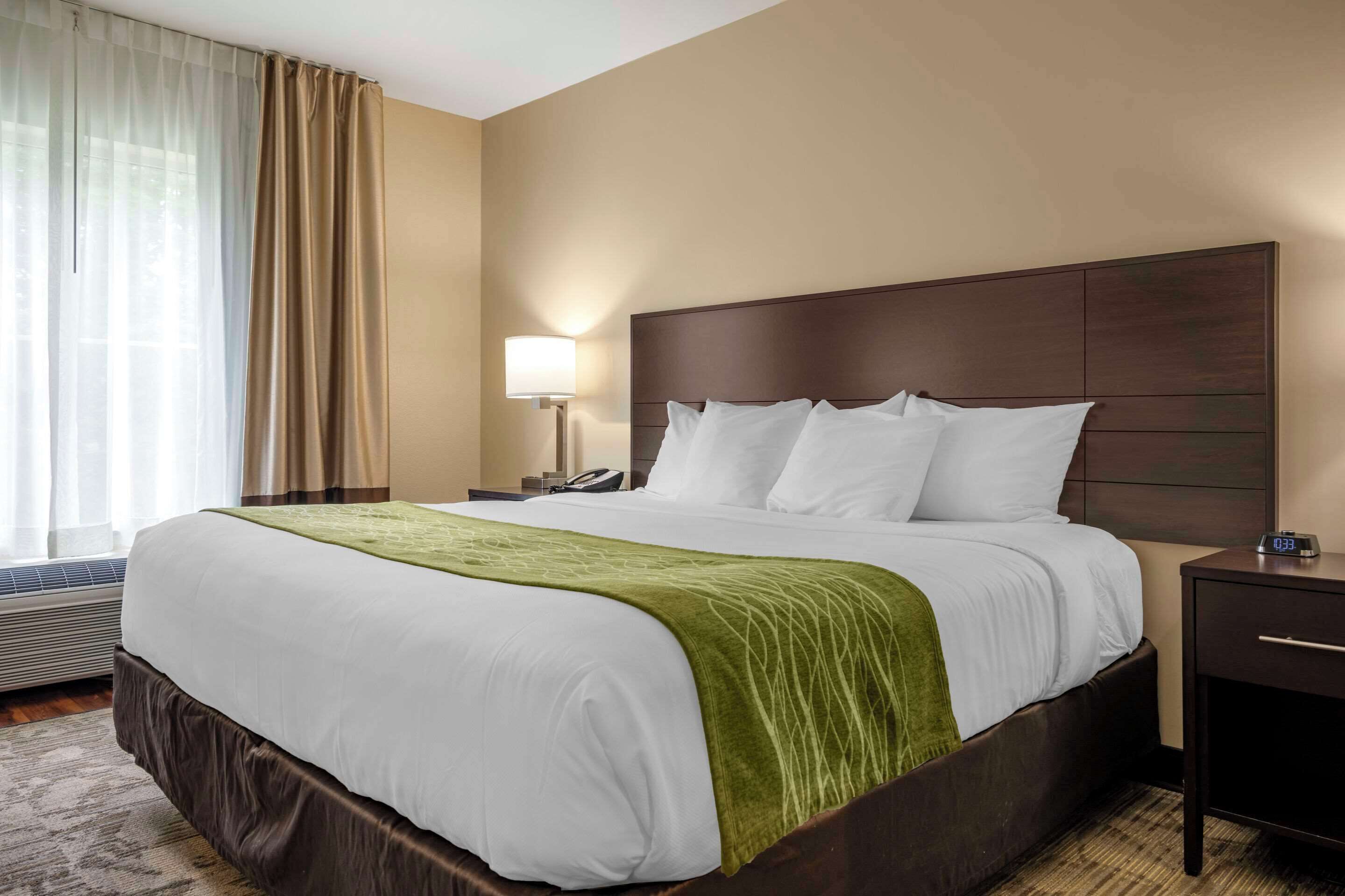 Une chambre d’hôtel avec un grand lit, une table de chevet avec une lampe et une petite table de nuit avec une horloge.