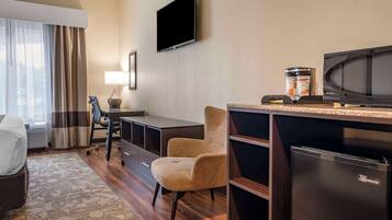 A hotel room with a desk, chair, television, microwave, and refrigerator.