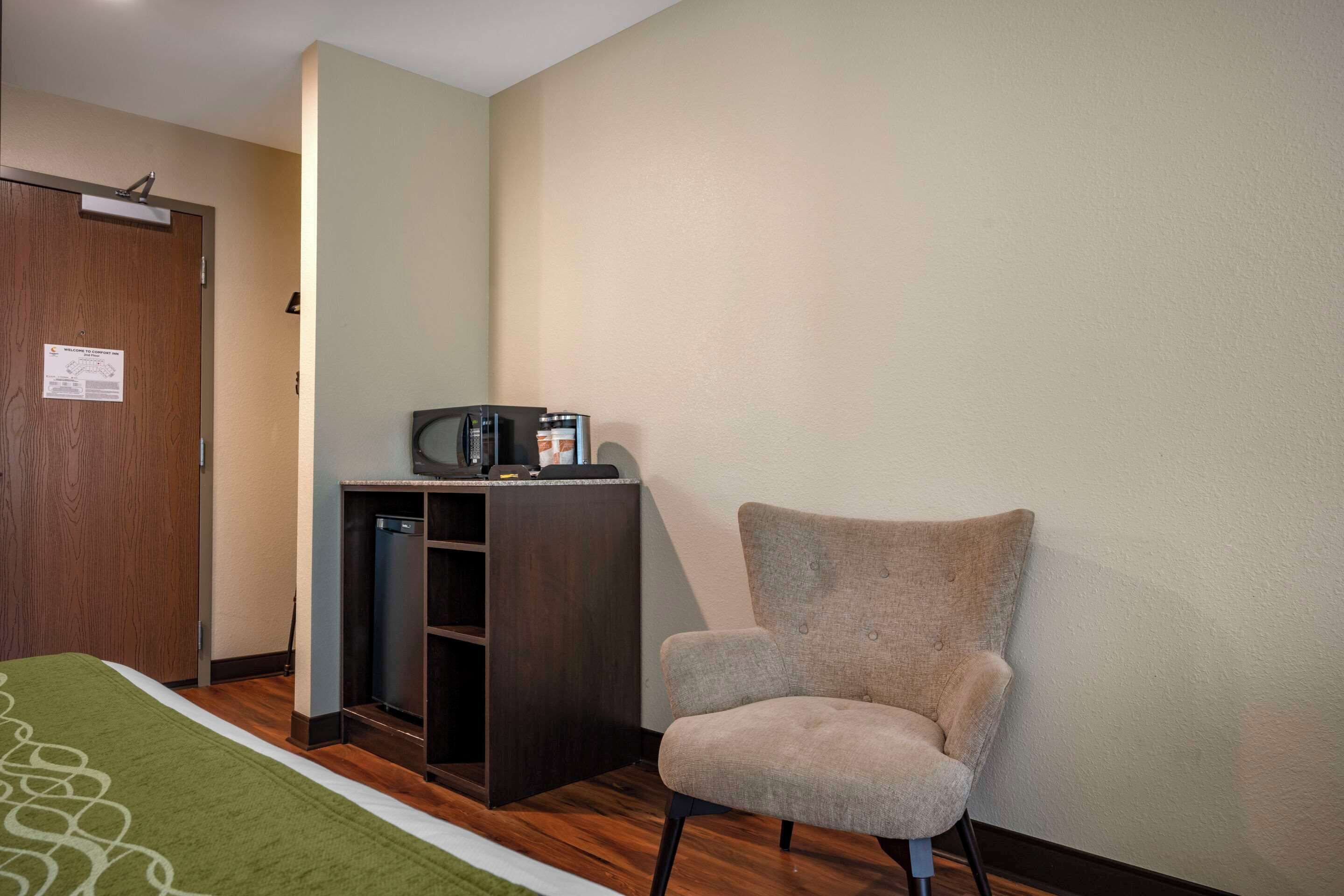 Une chambre d’hôtel avec un lit, une chaise, un bureau avec une machine à café et une porte.