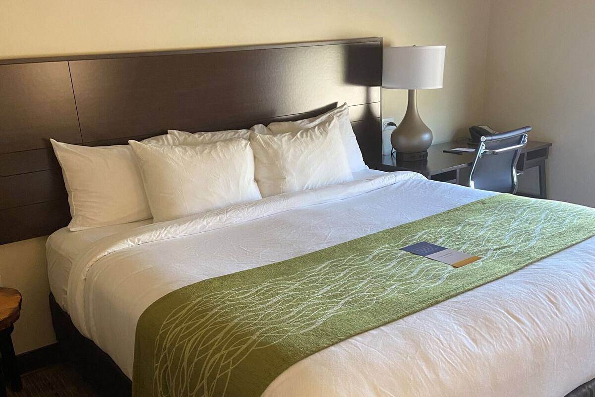 A hotel room with a large bed, a desk, a chair, a lamp, and a nightstand.