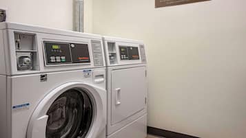 A row of white front-loading washers with digital displays, a notice sign, and a safety sign on the wall.